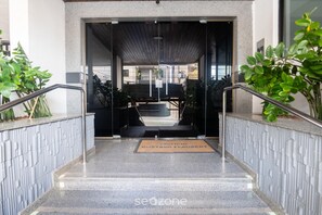 L’entrée d’un hôtel, avec une porte en verre, un paillasson et une rambarde en métal.