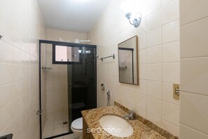 A bathroom with a glass shower enclosure, a toilet, a sink with a granite countertop, and a mirror on the wall.