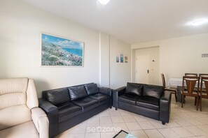 A living room with two black leather sofas, a beige armchair, a dining table with chairs, and a painting on the wall. - Apts in a Condominium 130m fr/ Morro Beach - Gfts (Guarapari)