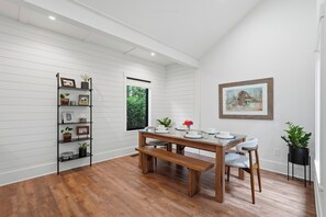 A dining area with a wooden table, benches, and a bookshelf. - Central extended stay cottage with a modern charm (Newberg)