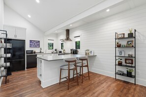 A modern kitchen with white cabinetry, a black refrigerator, wooden bar stools, and a black shelf with decorative items. - Central extended stay cottage with a modern charm (Newberg)