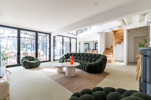 Ein modernes Wohnzimmer mit einem Ecksofa, einem runden Couchtisch und einem großen Fenster mit Blick ins Freie.