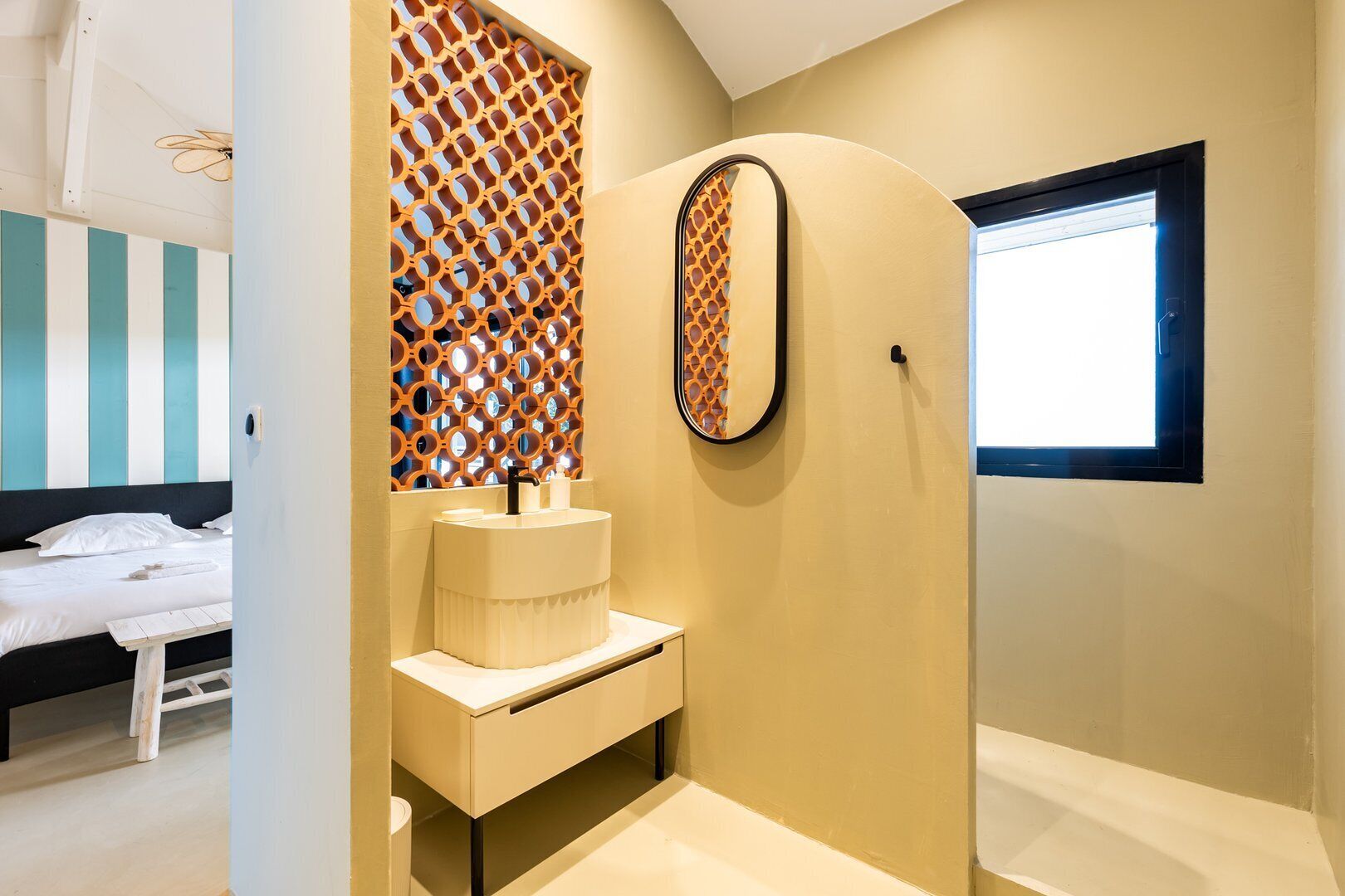 A modern bathroom with a built-in sink, a decorative lattice wall, and a large window.
