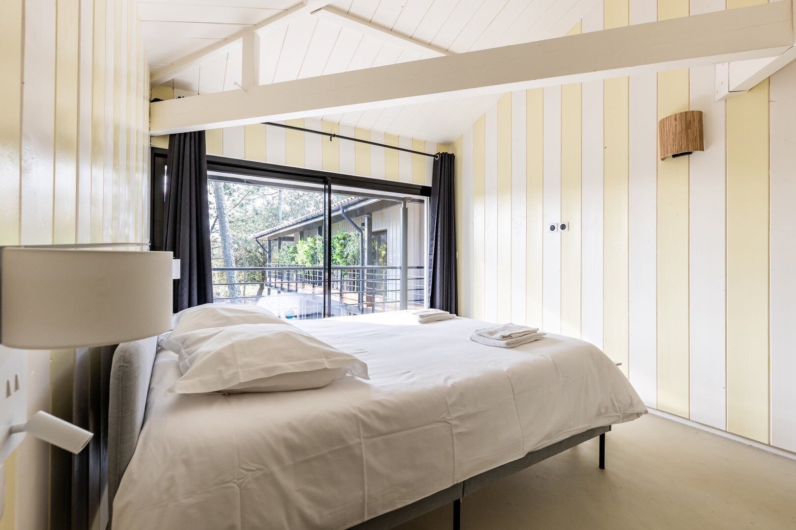 A bedroom with a bed, a window with curtains, and a view of a building outside.