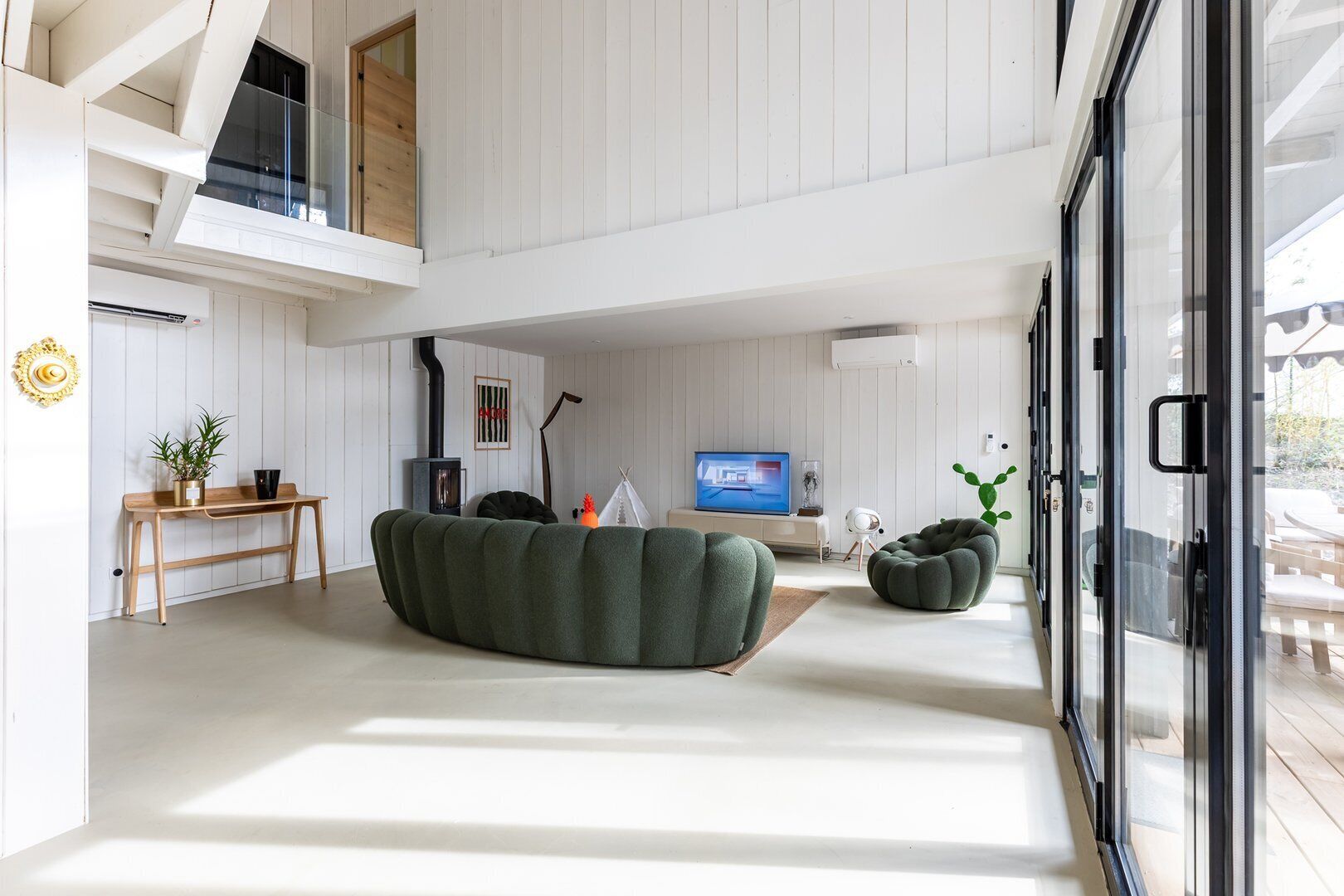A modern living room with a large green sofa, a wooden coffee table, a TV, and a glass door leading outside.