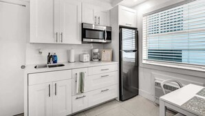 A compact kitchen with white cabinetry, a stainless steel refrigerator, a microwave, and a coffee maker. - Oceanfront Studio · South of Fifth + Beach Perks (Miami Beach)