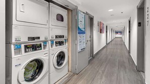 A hotel laundry room with multiple washing machines and dryers, a long corridor with doors numbered 227, and informational posters on the walls. - Oceanfront Studio · South of Fifth + Beach Perks (Miami Beach)