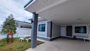 Een modern huis met een overdekte patio, een klein zitgedeelte buiten en een groot raam.