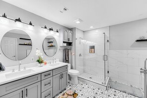 Une salle de bain moderne dotée d’un grand meuble-lavabo, de deux vasques, de toilettes et d’une douche à l’italienne.
