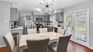A modern kitchen with a central island, built-in appliances, and a dining area with a marble table and chairs. - 5BR 2.5BA Spacious house sleeps 16 (Flower Mound)