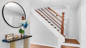 A staircase with wooden steps and a wooden handrail, leading to a landing with a marble console table and a mirror. - 5BR 2.5BA Spacious house sleeps 16 (Flower Mound)