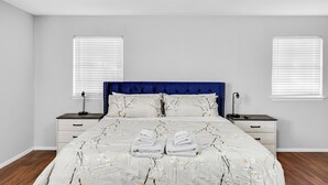 A bedroom with a bed, two bedside tables, and two windows with blinds. - 5BR 2.5BA Spacious house sleeps 16 (Flower Mound)