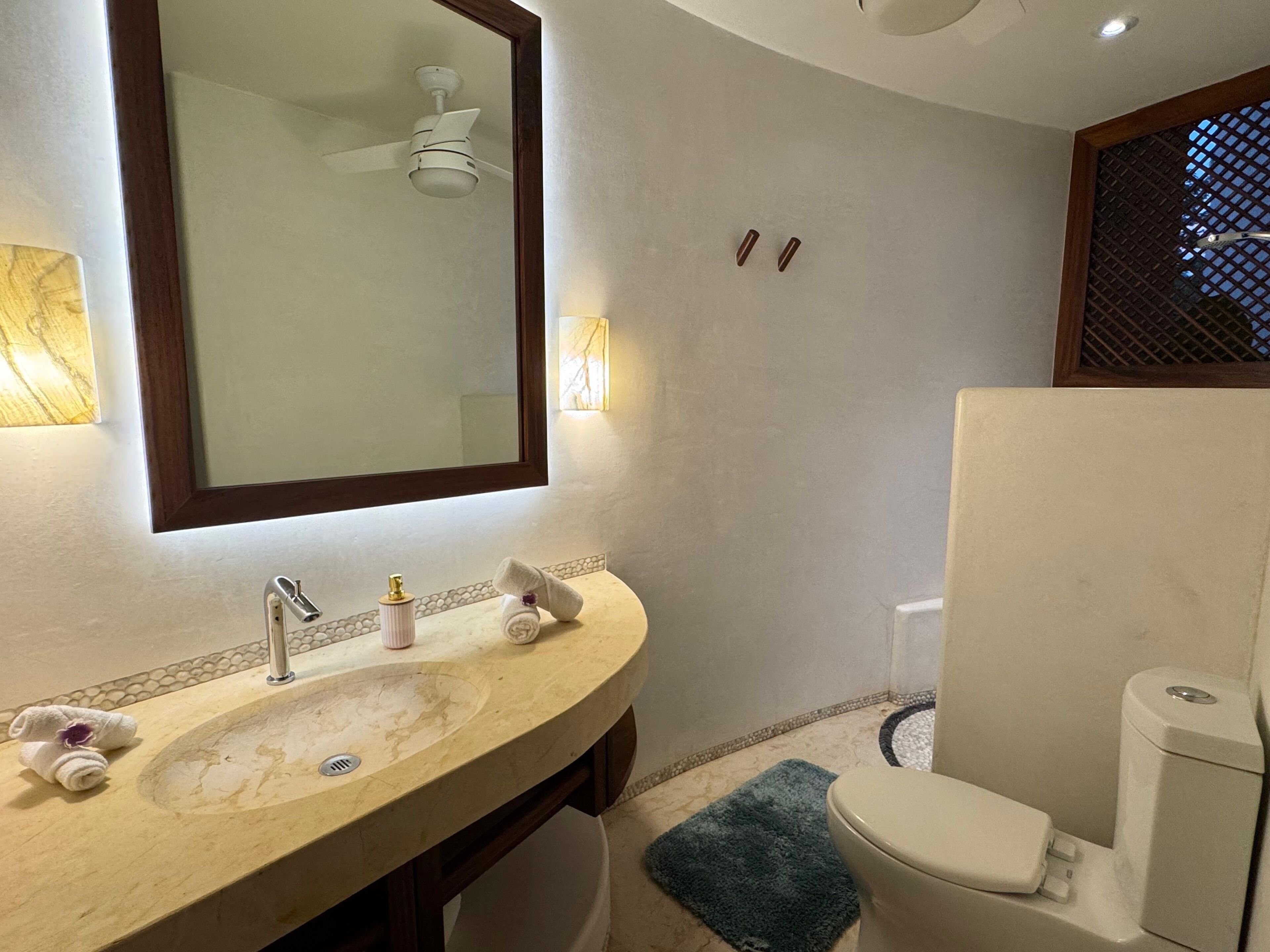 A bathroom with a large mirror, a sink, a toilet, and a ceiling fan.