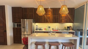 A modern kitchen with a central island, wooden slatted cabinets, stainless steel appliances, and pendant lighting. - Luxury Oceanfront At Majahua (Troncones)