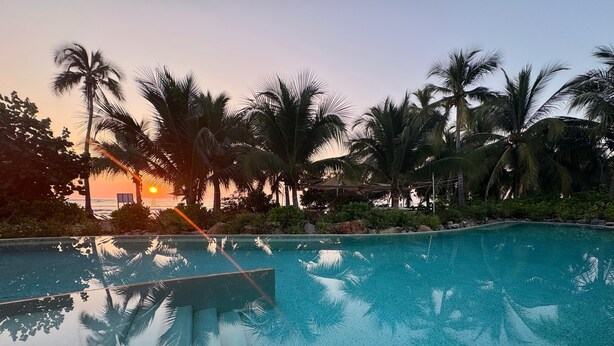 A clear swimming pool surrounded by palm trees and a sunset in the background. - Luxury Oceanfront At Majahua (Troncones)