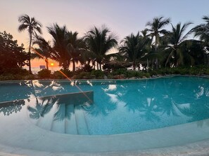 A clear swimming pool surrounded by palm trees and a sunset in the background. - Luxury Oceanfront At Majahua (Troncones)