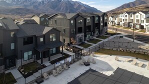 Un moderno complejo residencial con edificios de varios pisos, una zona de estar cubierta al aire libre y vistas a montañas nevadas al fondo.