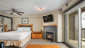 Ein Hotelzimmer mit einem Bett, einem Nachttisch aus Holz, einem Kamin, einem Fernseher und einer Glastür zum Außenbereich.