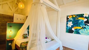 Een slaapkamer met een hemelbed, een schilderij van toekans en een houten vloer.