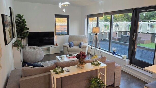 Un salon moderne doté d’un grand téléviseur à écran plat, de sièges confortables, d’une table basse et offrant une vue sur l’extérieur grâce à de grandes fenêtres.