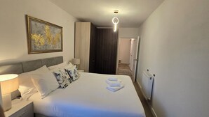 Une chambre d’hôtel avec un lit, une table de chevet, une lampe, un tableau et une porte donnant sur une autre pièce.