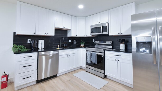 Una cocina moderna con armarios blancos, electrodomésticos de acero inoxidable y salpicadero negro.