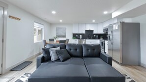 Una cocina moderna con armarios blancos, un refrigerador de acero inoxidable y un comedor con mesa y sillas.