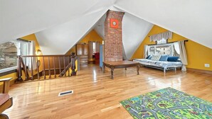 Un'ampia stanza mansardata con una scala in legno, un camino in mattoni e un letto con un tappeto colorato.