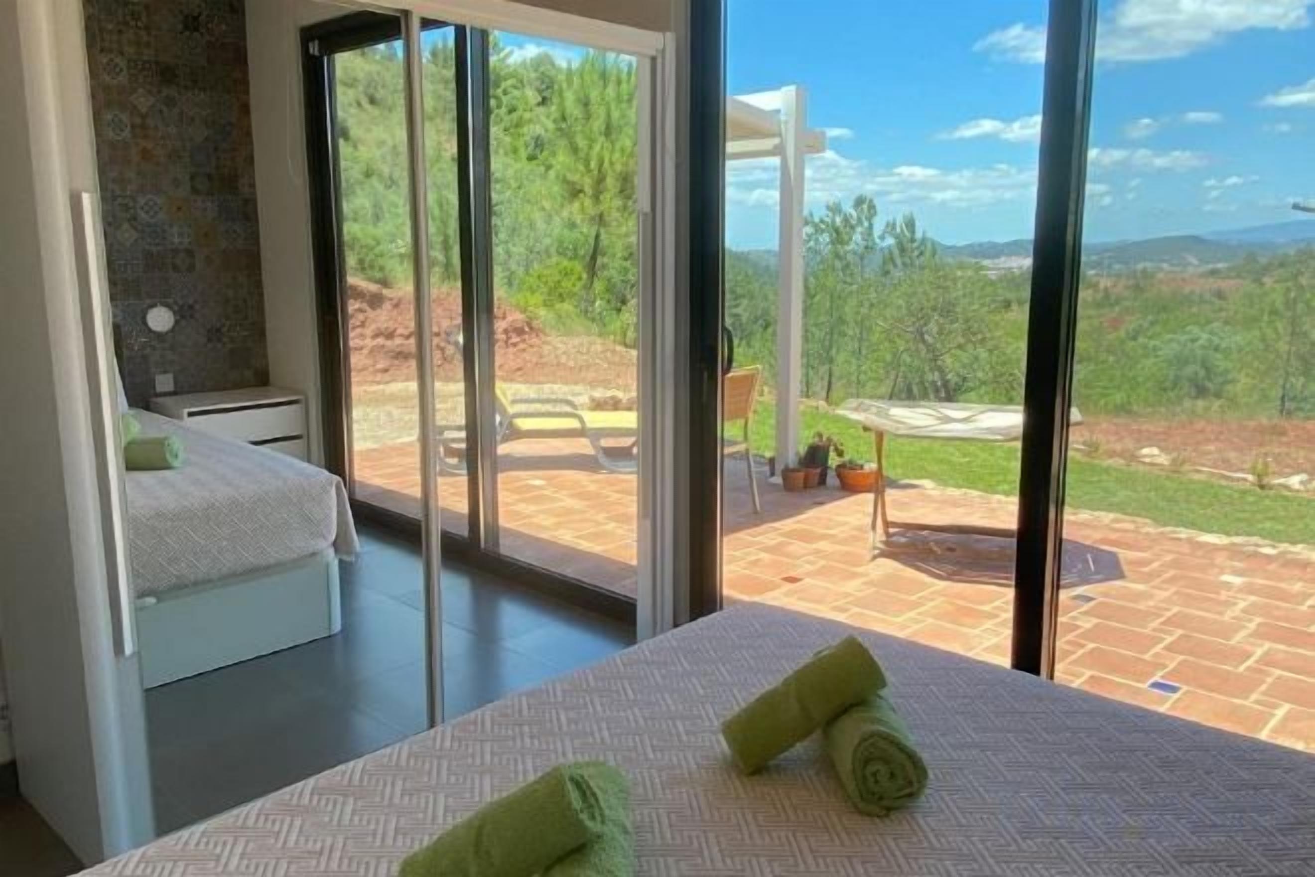 A bedroom with a bed, a nightstand, and a view of an outdoor patio with a table and chairs.