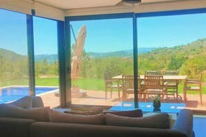 A room with a large window, a pool, and a dining area with outdoor furniture. - Casa Alfarobeira (Sao Bartolomeu de Messines)