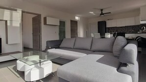 A modern living room with a grey sectional sofa, a glass coffee table, and ceiling fans.