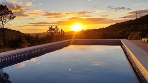 A swimming pool with a sunset view, surrounded by trees and hills.