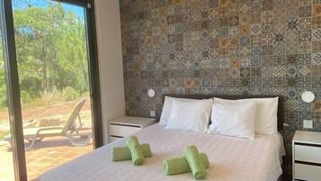A bedroom with a patterned wall, a bed with white linens, and a view of the outdoors.