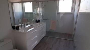 A modern bathroom with a large mirror, a white vanity, and a glass-enclosed shower.