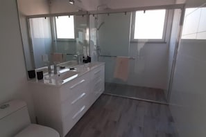 A modern bathroom with a large mirror, a white vanity, and a glass-enclosed shower. - Casa Alfarobeira (Sao Bartolomeu de Messines)
