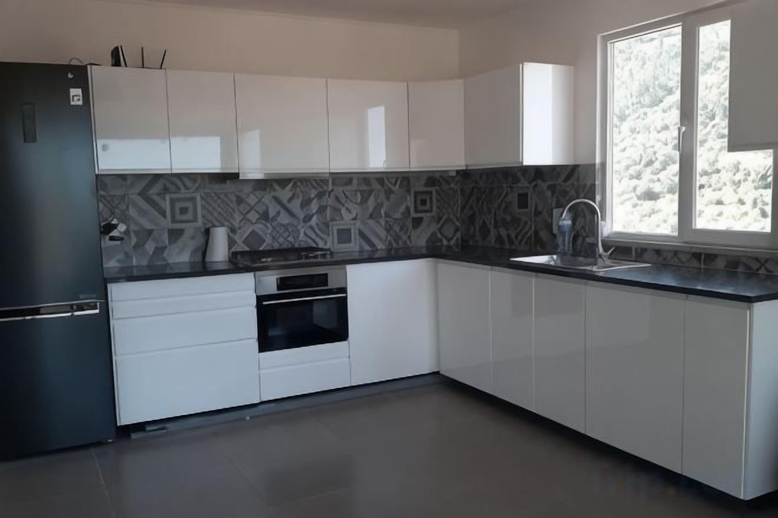 A modern kitchen with white cabinets, a black refrigerator, and a patterned backsplash.