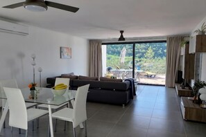 A modern living room with a glass dining table, white chairs, a dark sofa, and a large sliding glass door leading to an outdoor area. - Casa Diospiro (Sao Bartolomeu de Messines)