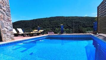 A swimming pool with lounge chairs and a view of a forested hill.