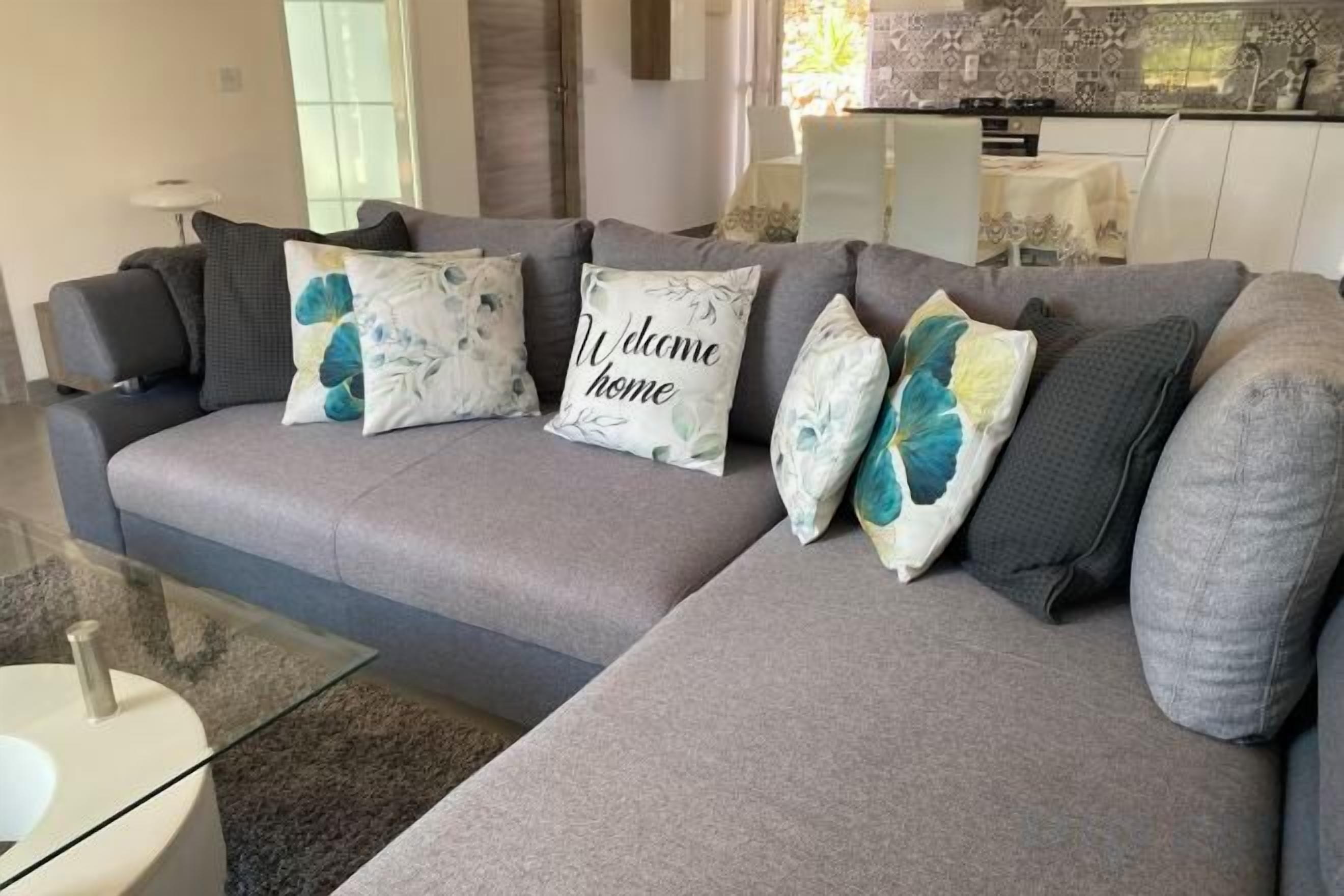 A grey sectional sofa with decorative pillows and a glass coffee table in a modern living room.
