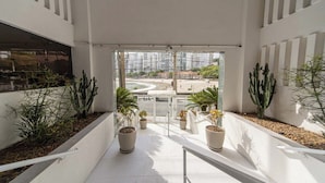 Ein modernes Interieur mit einer Glastür, die zu einem Außenbereich führt, mit Topfpflanzen und Blick auf eine Stadtlandschaft.