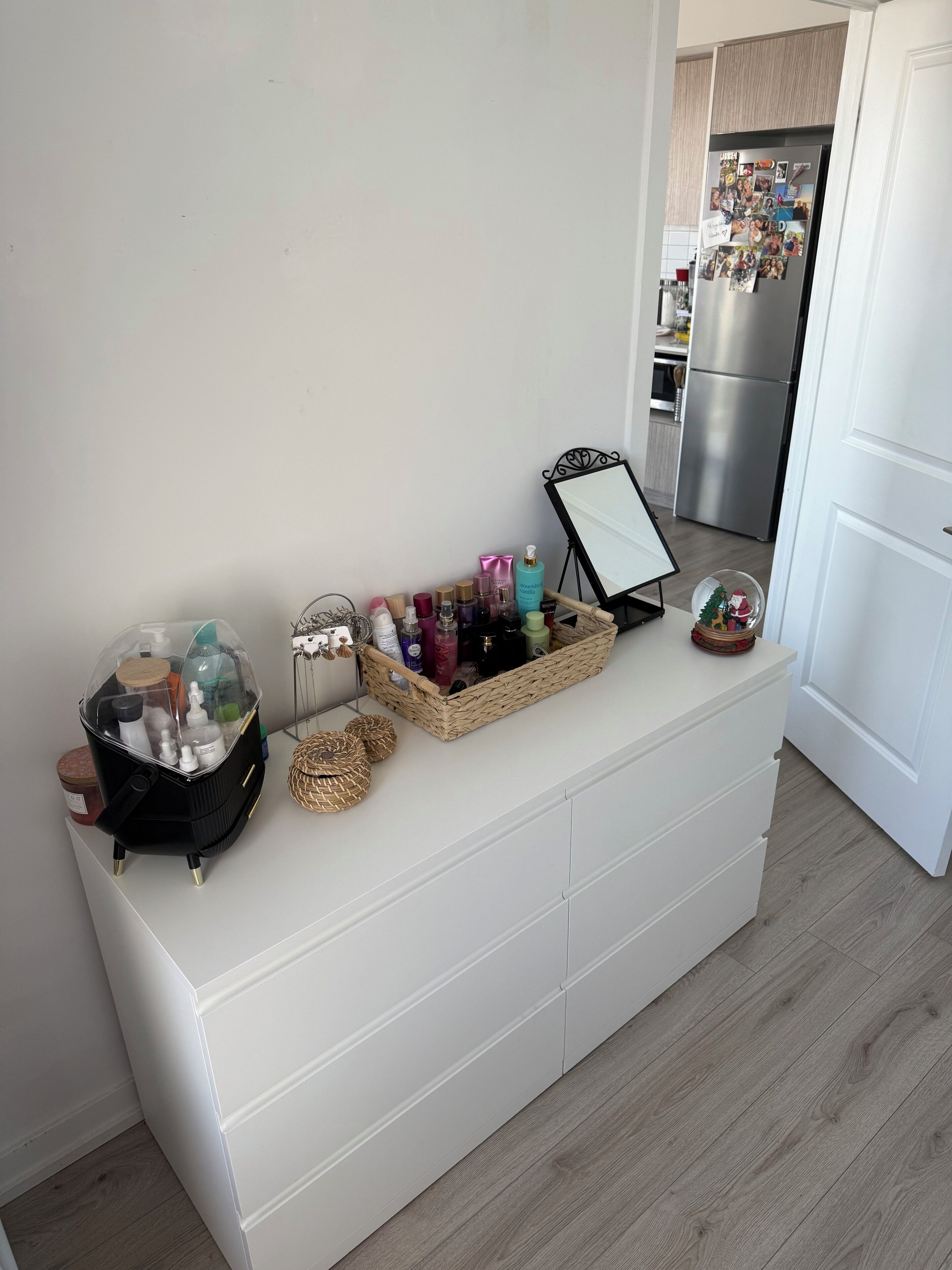 A white storage unit with a mirror, a basket of toiletries, and a decorative snow globe.