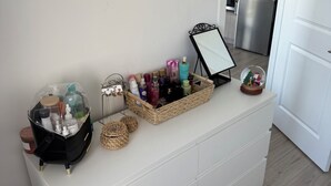 Un meuble de rangement blanc avec un miroir, un panier contenant des articles de toilette et un globe à neige décoratif.