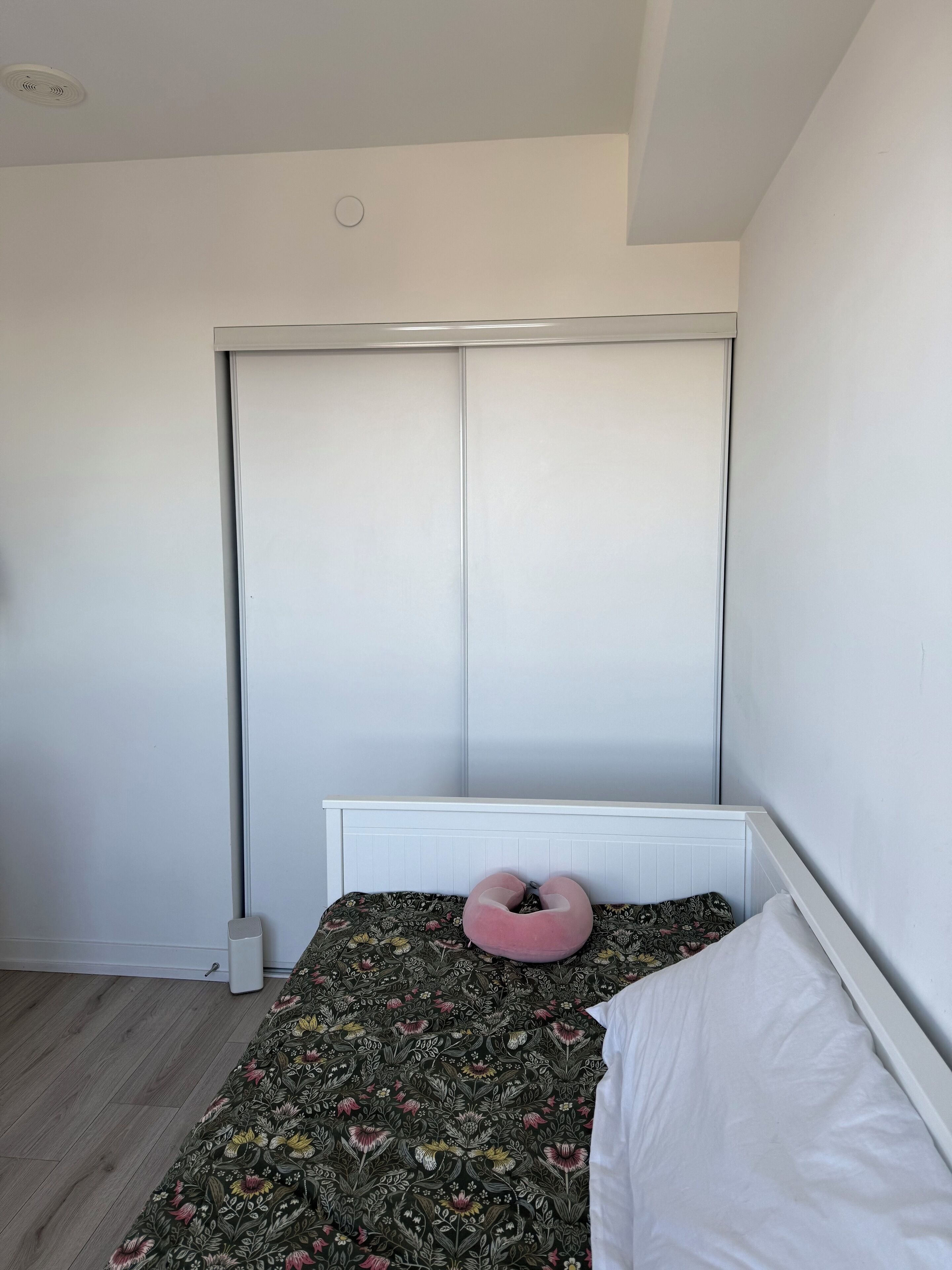 Ein Schlafzimmer mit einem Bett, einem weißen Kopfteil, einer blumigen Tagesdecke, einem rosafarbenen Kissen und einem weißen Heizkörper.