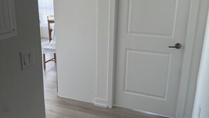 Un couloir avec une porte blanche, un plancher en bois et un paillasson noir.