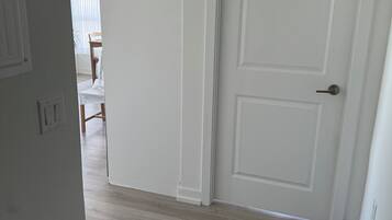Un couloir avec une porte blanche, un plancher en bois et un paillasson noir.
