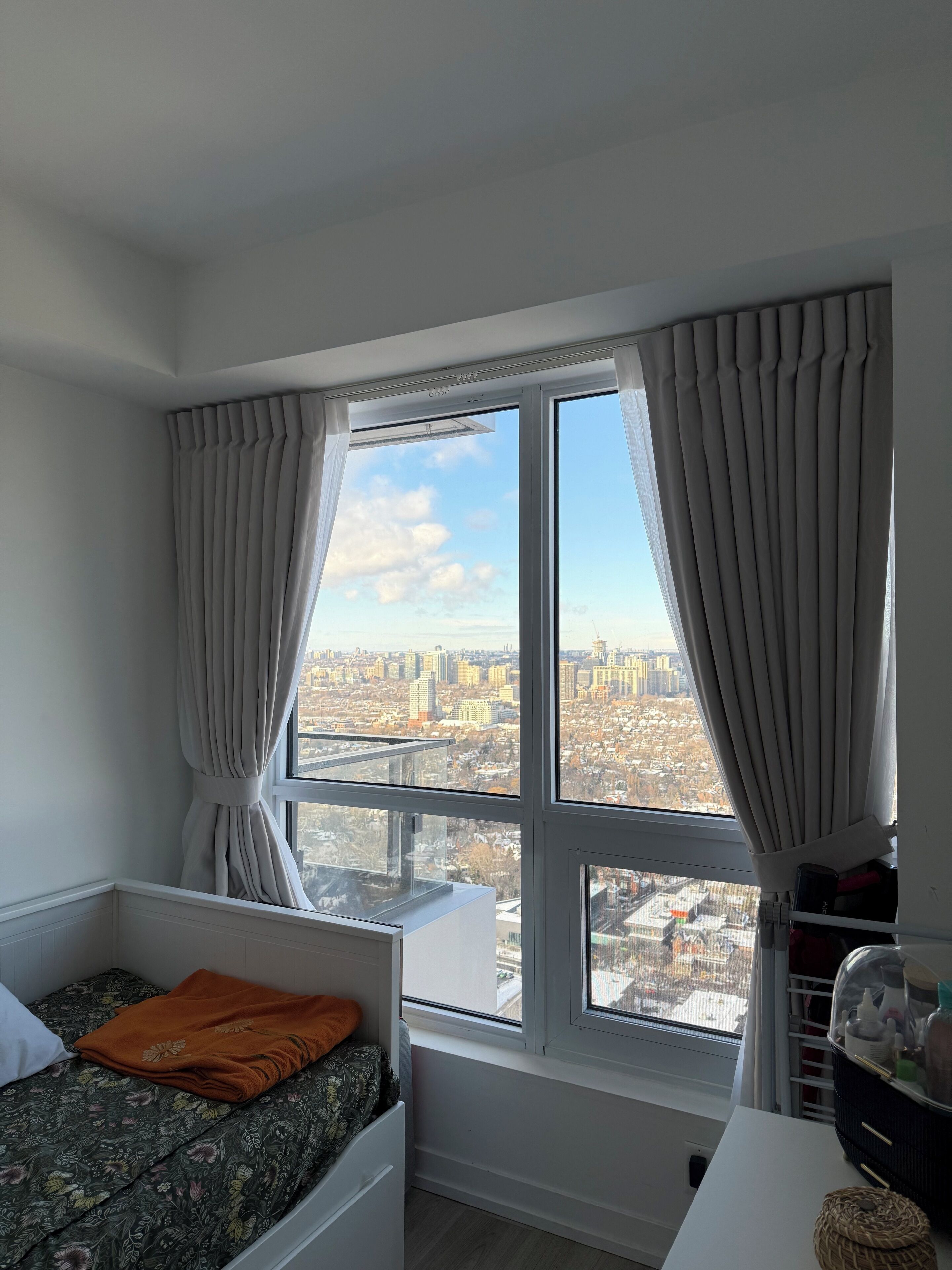 Une chambre avec vue sur la ville, un lit avec un oreiller orange et une fenêtre avec des rideaux.