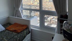 Une chambre avec vue sur la ville, un lit avec un oreiller orange et une fenêtre avec des rideaux.