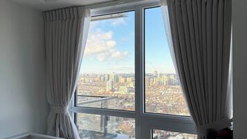 Une chambre avec vue sur la ville, un lit avec un oreiller orange et une fenêtre avec des rideaux.