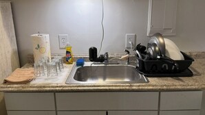 Eine Küche mit einem Edelstahl-Spülbecken, einer Arbeitsplatte mit Geschirrgestell, einer Küchenpapierrolle und einer Flasche Spülmittel.