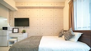 Un dormitorio moderno con cama, televisor de pantalla plana en la pared, escritorio con silla y ventana con cortinas.